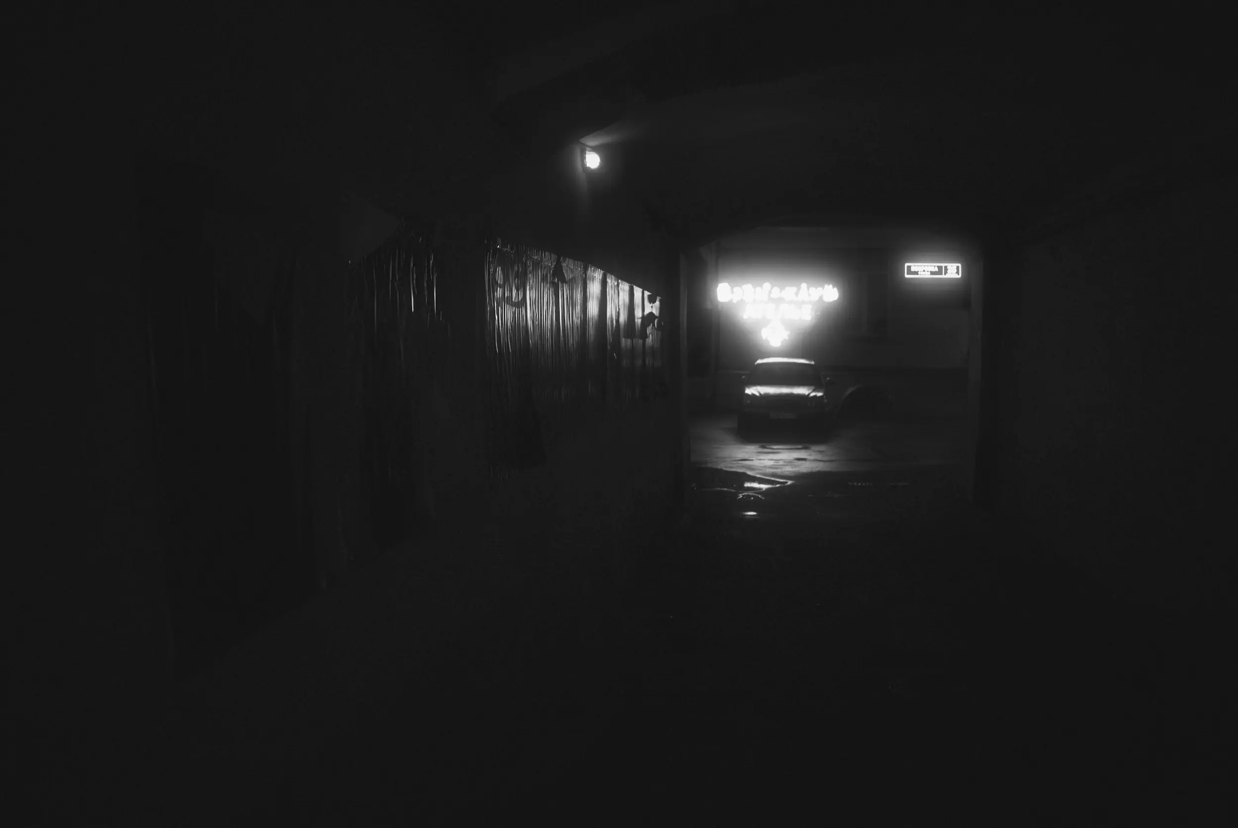 Black and white high-contrast photo with a silhouette of a car and a sign pointing to it from above